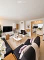 Modern living room with a dark grey sectional sofa, white coffee table, fireplace, flat-screen TV, and decorative plants.