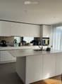 Modern kitchen with white cabinets, a central island, and a sink. Appliances and small items are visible on the counter.