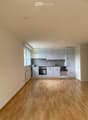 Empty kitchen with light grey cabinets, wooden floor, and a window on the left side.