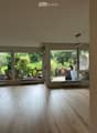Empty room with light wooden flooring, large windows, and sliding glass doors leading to a garden area.