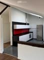 Modern kitchen with white cabinets, stainless steel appliances, and a red backsplash. The space features wooden flooring and exposed wooden beams.