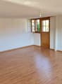 Empty room with light wooden flooring, white walls, and a wooden door leading to another space.