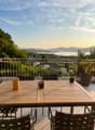 Balcony with wooden table, black chairs, and scenic view of a lake and mountains.