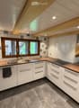 Modern kitchen with white cabinets, wooden countertops, stainless steel sink, and built-in stove. Features exposed wooden beams on the ceiling and large windows.