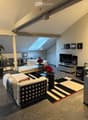 Modern living room with white sofa, coffee table, TV, floor lamp, bookshelf, and potted plants. Features a skylight and contemporary decor.