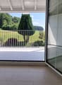 Open sliding glass doors lead to a balcony with a view of a green field and trees.