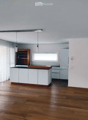 Modern kitchen with white cabinets, wooden countertop, and pendant lights. Features a wooden shelf, a sink with a faucet, and a refrigerator. The space is illuminated by natural light from a window covered with sheer curtains.