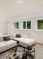 Modern living room with white walls, large windows, grey sectional sofa, coffee table, and decorative plants.