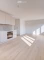Modern kitchen with white cabinets, light wooden flooring, and large windows allowing natural light to fill the space. Features include a sink, faucet, and built-in oven.