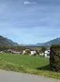 A peaceful rural landscape with a cluster of houses, green fields, and distant mountains under a clear blue sky.