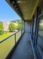 Balcony with concrete floor, glass railing, and view of green park and buildings.