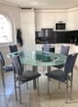 Modern kitchen with white cabinets, a glass dining table surrounded by four grey chairs, and a microwave on the counter.