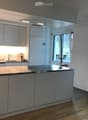 Modern kitchen with white cabinetry, a central island, and a sink area. Features include a candle holder on the island, a window with dark curtains, and built-in lighting.