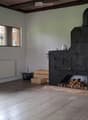 Bright room with wooden flooring, white walls, a wood stove, radiator, and a basket with wood logs.