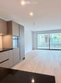 Open-plan kitchen and living area with light wood flooring, modern cabinetry, and large glass sliding doors leading to an outdoor space.