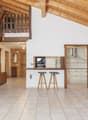 Open-plan living and dining area with a wooden staircase leading to an upper level, a kitchen area with cabinets and a range hood, and two stools at a kitchen island.