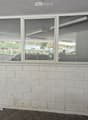 Corner of a building with white brick walls and large windows, showing reflections of parked cars and outdoor area.