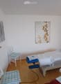 A small, well-lit room with a treatment table, two chairs, and artwork on the walls.