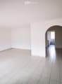 Empty room with white tiled floor and walls, featuring an arched doorway leading to a small bathroom with white tiles and a sink.