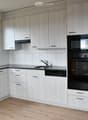 Modern kitchen with white cabinets, black appliances, and a wooden floor. Features a sink, microwave, oven, refrigerator, and dishwasher.