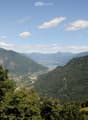 Panoramic mountain view with lush green forests, a lake, and a town nestled in the valley below.