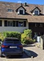 Two-story house with a tiled roof, multiple windows, and a garage. A blue car is parked in the driveway.