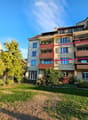 Multi-story residential building with multiple balconies, surrounded by greenery and a lawn.