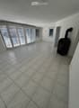 Empty room with tiled floor, large windows with blinds, and a small black stove in the corner.