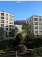 Modern multi-story residential building with white facade, large windows, and surrounding greenery.
