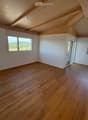 Empty room with wooden flooring, white walls, and large windows offering a scenic view. The ceiling features exposed wooden beams.