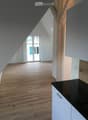 An unfurnished attic room with wooden flooring, white walls, and a sliding glass door leading to a balcony.