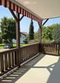 wooden railing, red and white striped awning, view of a grassy area with trees and houses