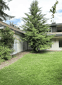Two-story house with a pitched roof, surrounded by greenery and a well-maintained lawn.