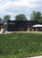 Modern commercial building with a black facade, signage for "Neff AG" and "Tenne Grill", outdoor seating area, and a grassy lawn in front.