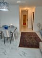 Modern hallway with marble flooring, a patterned rug, and a dining area visible to the left, featuring a grey table, chairs, and a decorative bowl.