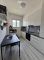 Modern kitchen with white cabinets, dark countertops, and a dining area featuring a table and chairs. The kitchen includes an oven, sink, and various appliances.
