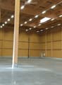 Empty warehouse space with wooden walls, concrete floor, exposed wooden beams, and a large garage door.