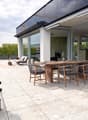 Modern rooftop terrace with a wooden dining table, six chairs, a lounge chair, a small side table, and a potted tree.