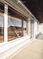 Spacious balcony with large windows, wooden flooring, and a view of the surrounding landscape.
