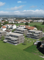 Aerial view of a residential area with modern apartment buildings, green lawns, and surrounding town with houses and fields.