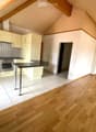 Bright, modern kitchen with light-colored cabinets, stainless steel appliances, and a central island. The space features a mix of tiled and wooden flooring, with a doorway leading to another room.