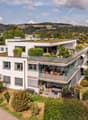 Modern white house with large windows, green roof, and surrounding garden with outdoor seating area.