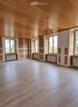 Empty room with wooden flooring and wooden ceiling, large windows with radiators below, and exposed wooden beams on the ceiling.