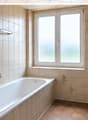 Bathroom with beige tiles, a bathtub, a sink, a toilet, and a window with frosted glass. The walls have decorative floral tiles, and there is a mirror above the sink.