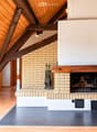 Modern living room with exposed wooden beams, skylight, and a brick fireplace with tools nearby.