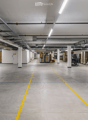 Large, empty warehouse or industrial space with concrete floors, white walls, and visible storage racks and pallets.