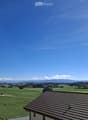 A panoramic view of a lush green field with scattered trees and distant mountains under a clear blue sky.