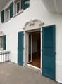 Balcony with metal railing, green shutters, and a view of the house entrance and surrounding greenery.