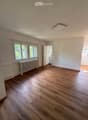 Empty room with wooden flooring, white walls, large windows, radiator, and a door leading to another room.