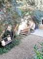 a cozy garden with bench, trees, greenery, stone pathways, and stone house in the background